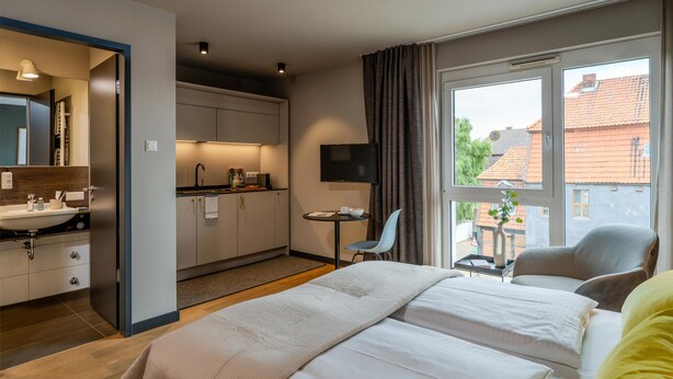 A hotel room with a bed, a desk, a TV, and a view of the outside. - ipartment Wolfsburg @HOME by Best Western (Wolfsburg)