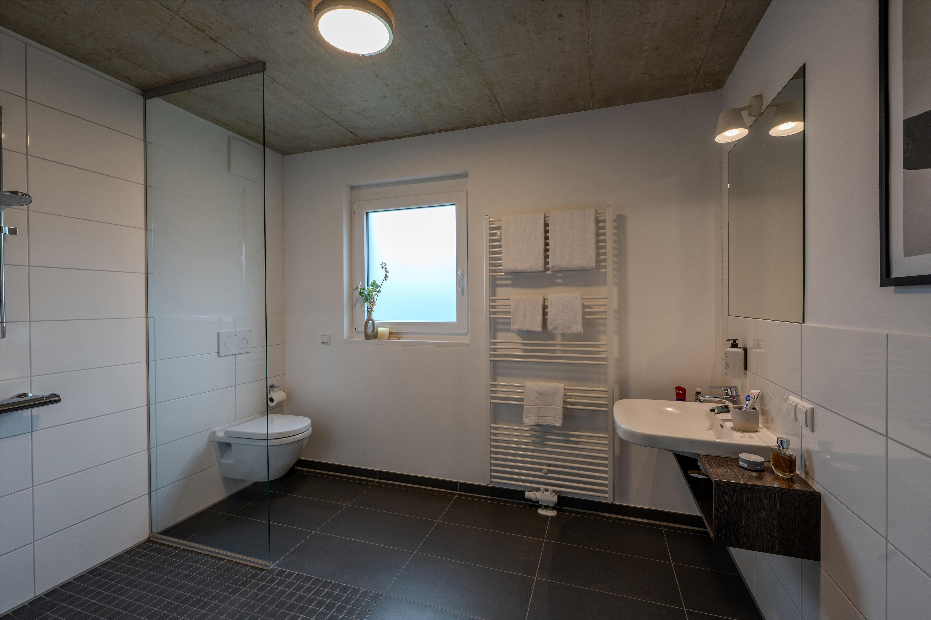 Un baño moderno con cabina de ducha de vidrio, inodoro, lavamanos con espejo y ventana.