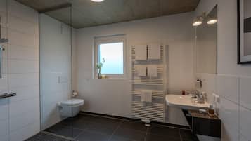 Un baño moderno con cabina de ducha de vidrio, inodoro, lavamanos con espejo y ventana.