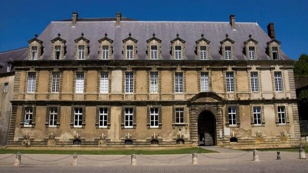 Un grand bâtiment historique à la façade symétrique, doté de nombreuses fenêtres et d’une entrée centrale.