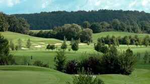 Un parcours de golf avec des collines verdoyantes, des arbres et une forêt en arrière-plan.