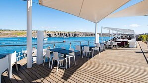 Una terraza de madera con mobiliario exterior, una piscina y vistas a acantilados.
