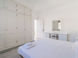 A bedroom with a large wardrobe, a vanity with a mirror, and a neatly made bed.