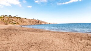 Una playa con arena y un acantilado rocoso al fondo.