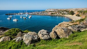 Una marina costera con barcos, una playa arenosa y un pueblo al fondo.