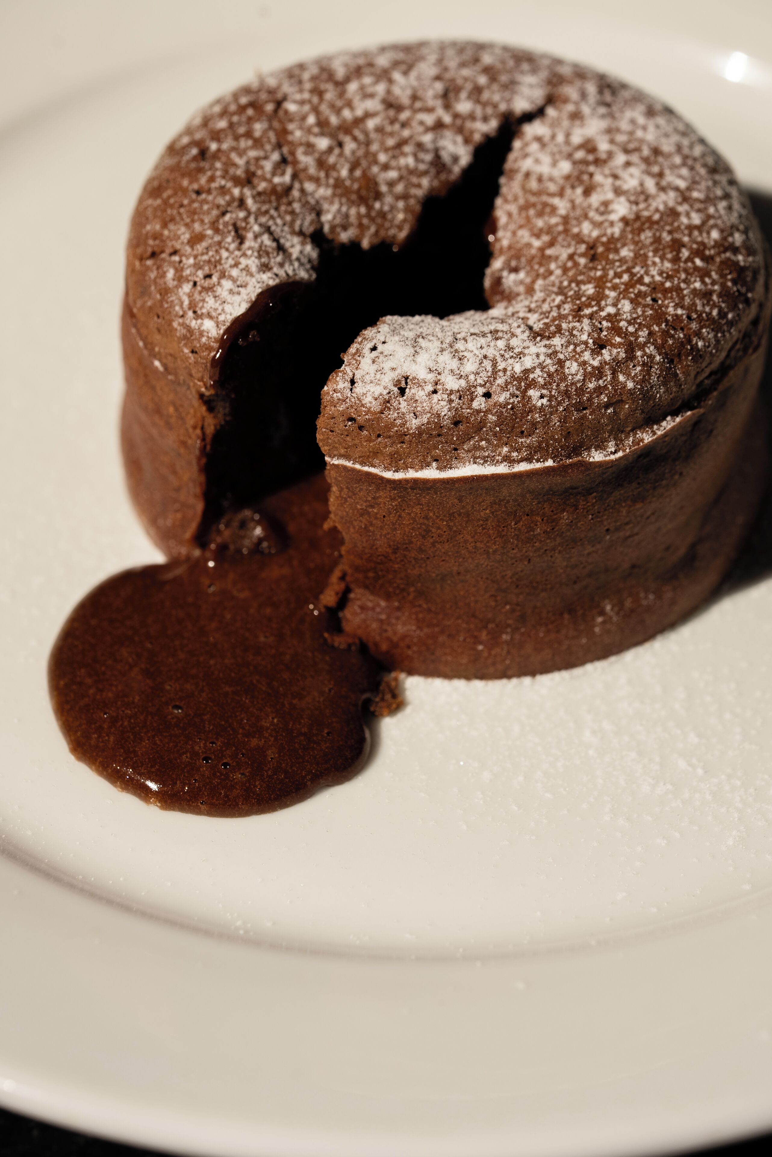 Ein Schokoladen-Lava-Kuchen mit einem Riss in der Mitte und einem Klecks Soße auf einem weißen Teller.