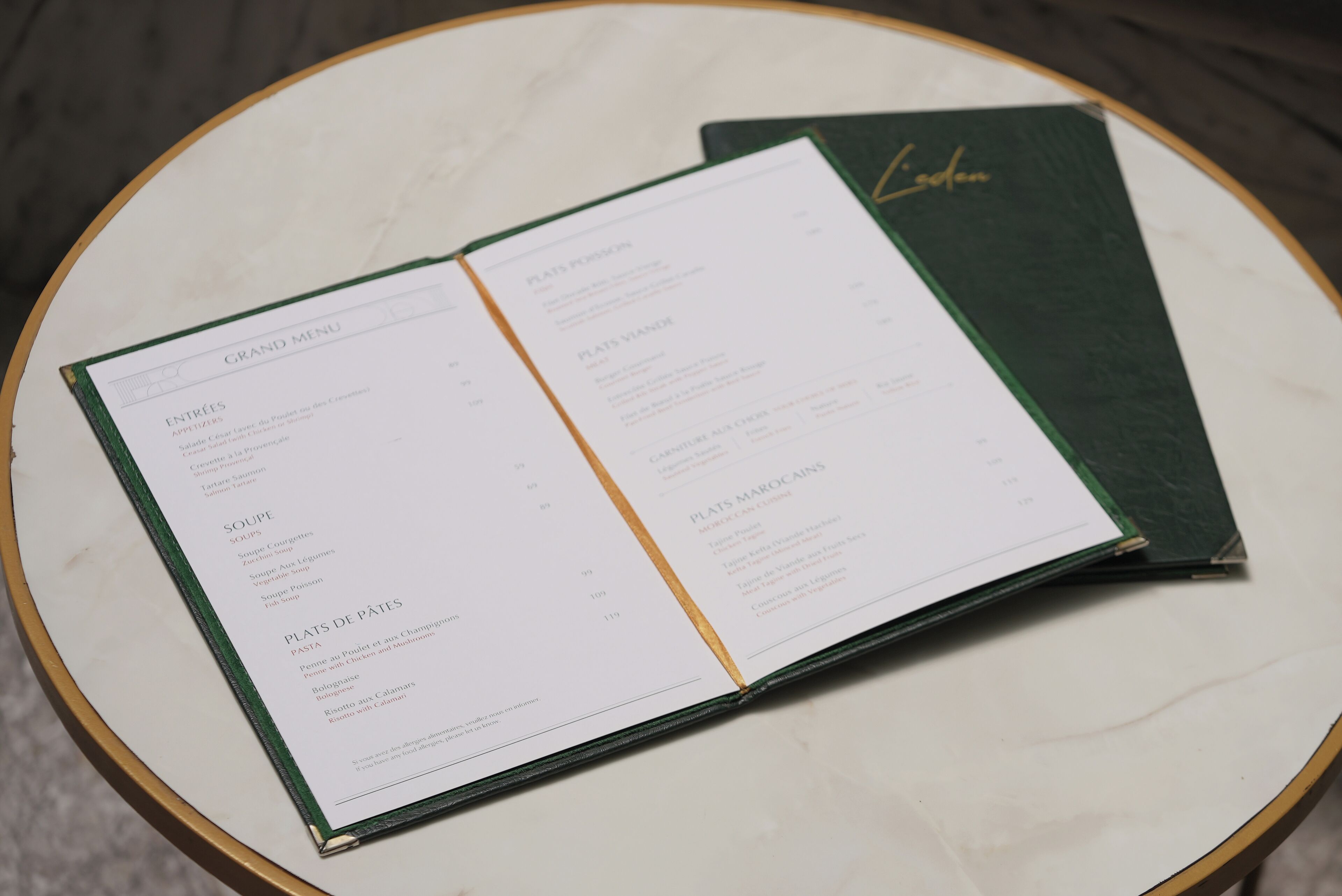 Un menu ouvert est posé sur une table ronde recouverte d’une nappe verte.