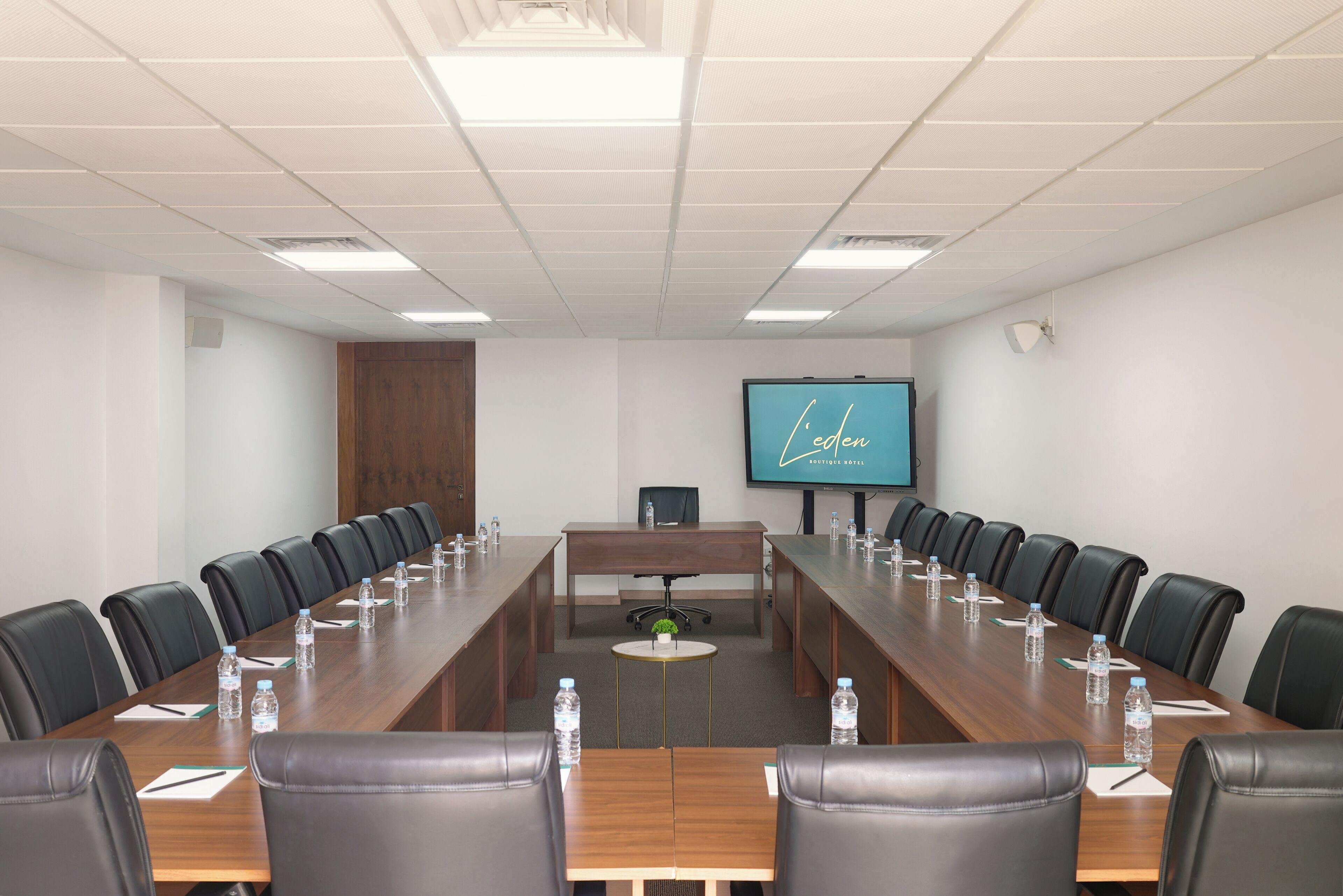 A conference room with a long table, chairs, water bottles, and a TV screen displaying 'Leben'.