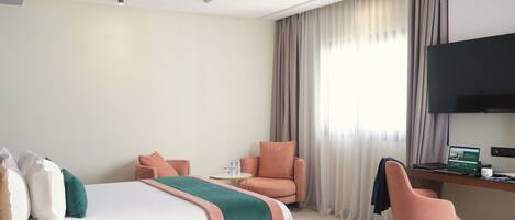 A hotel room with a bed, two chairs, a desk with a laptop, and a TV.