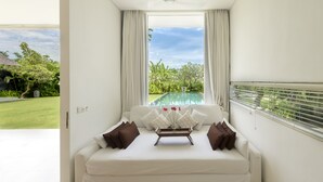 A modern room with a white sofa, a tray with flowers, and a view of a swimming pool and greenery. - Villa Kavya (Canggu)