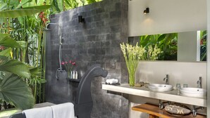 A modern bathroom with a stone shower, a large mirror, and a wooden vanity. - Villa Kavya (Canggu)