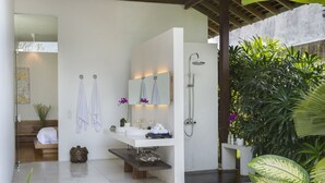 A modern bathroom with a large mirror, two sinks, a shower, and a bench. - Villa Kavya (Canggu)