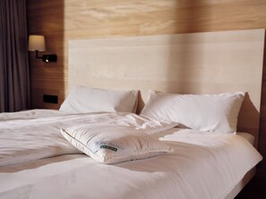 A hotel room with a neatly made bed, a headboard, and a wall-mounted lamp. - Peterhof Chalets (Zwischenwasser)