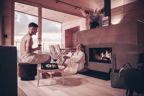 A modern interior with a fireplace, wooden flooring, and a large window. - Peterhof Chalets (Zwischenwasser)