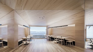 A modern interior with wooden flooring, tables, chairs, and large windows offering a view of the outdoors. - Peterhof Chalets (Zwischenwasser)