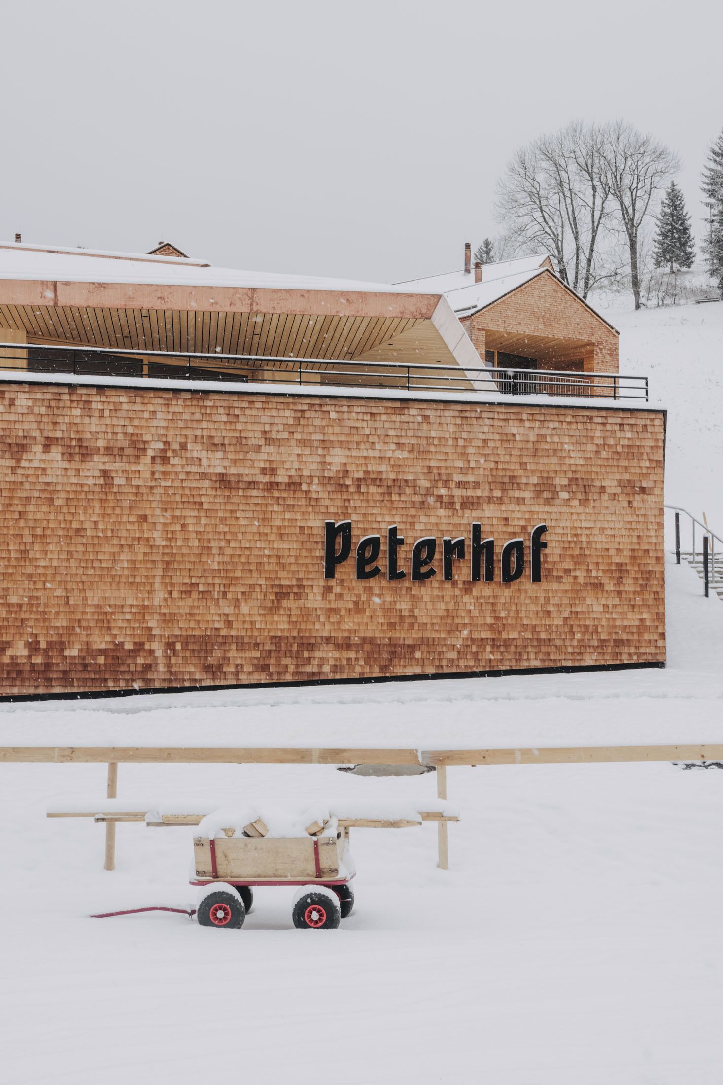 Un mur extérieur recouvert de neige, sur lequel on peut lire le nom « Peterhof », et un chariot en bois avec une corde rouge.