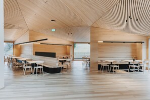 A modern interior with wooden panel ceilings, multiple seating areas, and large windows. - Peterhof Chalets (Zwischenwasser)