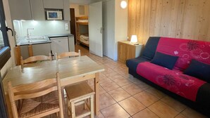 A compact living space with a kitchenette, a dining table with chairs, a sofa, and a small bedside table with a lamp. - Quiet studio for 4 pers. with terrace in Samoëns (Samoëns)