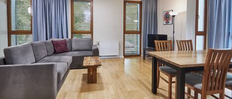 A modern living room with a grey sofa, wooden coffee table, and a dining area with a wooden table and chairs.