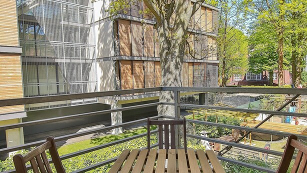 An outdoor seating area with wooden tables and chairs, surrounded by a metal railing, overlooking a garden and buildings. - Apartamenty Swinoujscie - Villa Stil II (Swinoujscie)