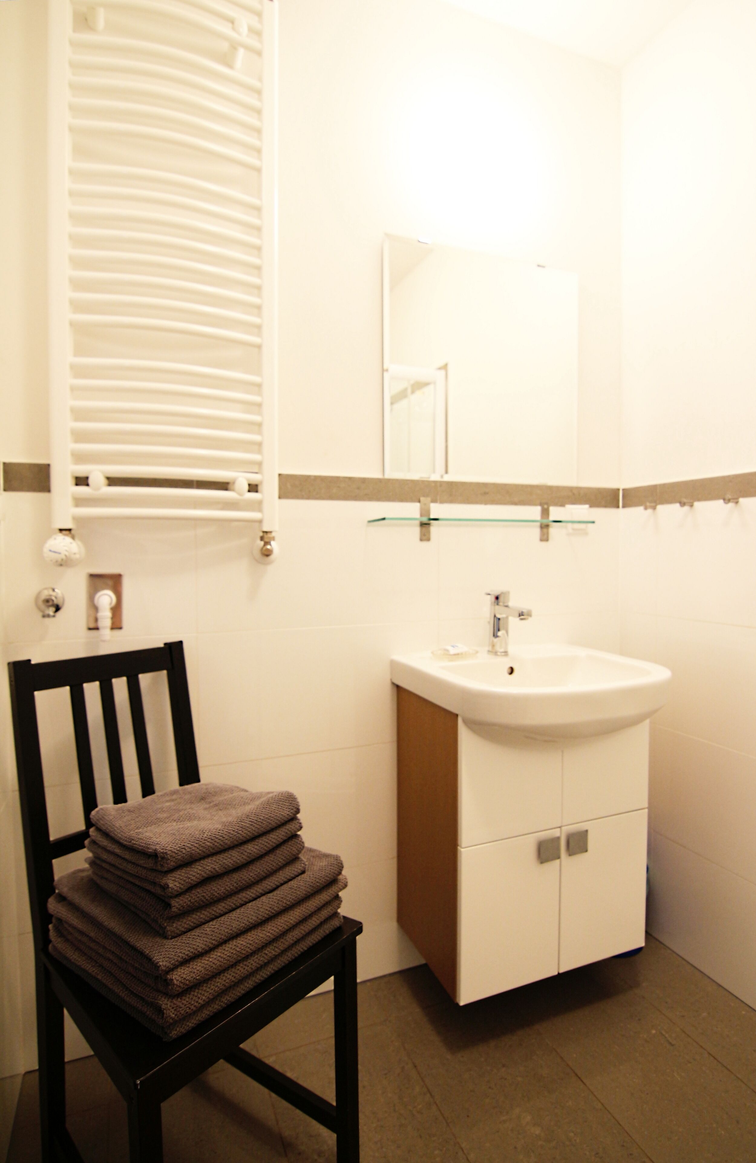 A bathroom with a sink, mirror, towel stack, and a radiator.