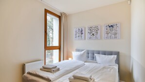 A neatly made bed with white linens and towels, a window with curtains, and three botanical-themed wall art pieces. - Apartamenty Swinoujscie - Villa Stil II (Swinoujscie)
