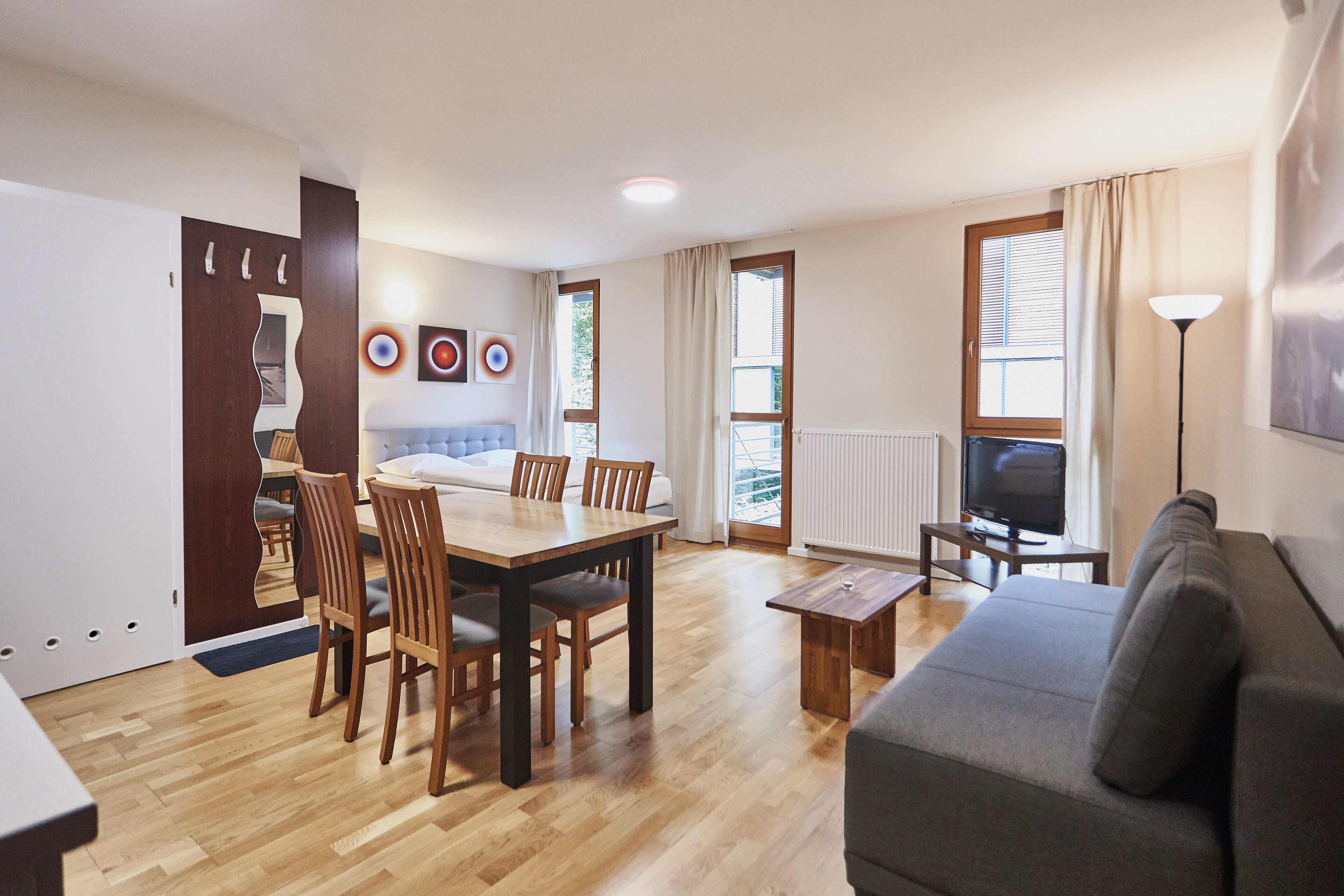 Un salon moderne comprenant un canapé, une table à manger avec des chaises, un téléviseur et une grande fenêtre avec des rideaux.
