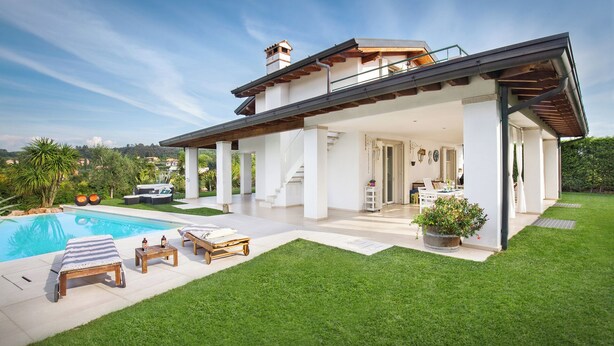 A modern house with a covered patio, a swimming pool, and a well-maintained lawn.