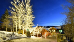 Paesaggio innevato con un rifugio dalle pareti in pietra e strutture in legno, illuminato da luci a stringa.
