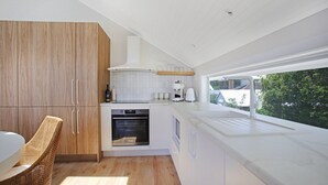 A modern kitchen with wooden cabinets, a built-in oven, a coffee machine, and a large window offering a view of greenery outside. - Tea Gardens Loft - Boutique Accommodation (Tea Gardens)