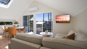 A cozy living room with a sofa, a dining table with chairs, and a balcony with a view of the outside. - Tea Gardens Loft - Boutique Accommodation (Tea Gardens)