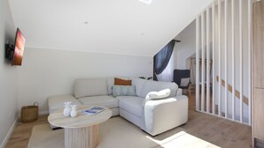 A modern living room with a sectional sofa, a round coffee table, and a staircase with a wooden railing. - Tea Gardens Loft - Boutique Accommodation (Tea Gardens)