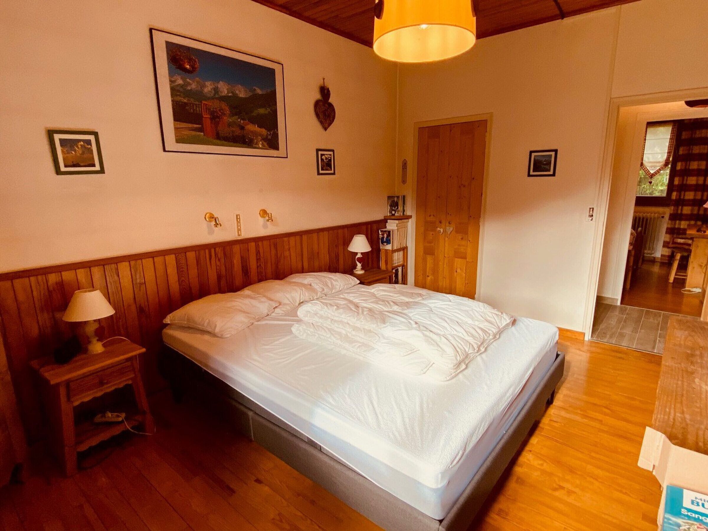 A bedroom with a wooden headboard, a bed with white bedding, a nightstand with a lamp, a wooden door, and a framed picture on the wall.