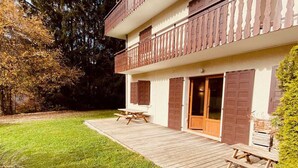 En toetages bygning med en træterrasse, en overdækket terrasse og en græsplæne.