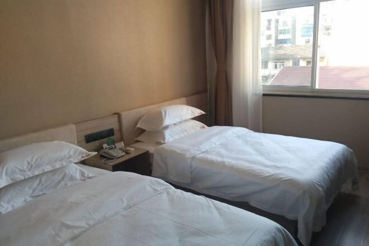 Une chambre d’hôtel avec deux lits, une table de chevet avec une lampe et une fenêtre donnant sur des immeubles.