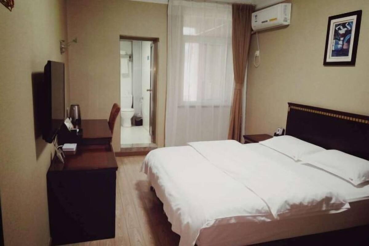 Une chambre d’hôtel équipée d’un lit, d’un bureau, d’une chaise, d’un appareil de climatisation et d’une porte donnant accès à une salle de bain.