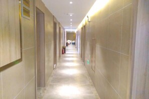 Un largo y estrecho pasillo de hotel con puertas a ambos lados, iluminación empotrada y suelo de baldosas.