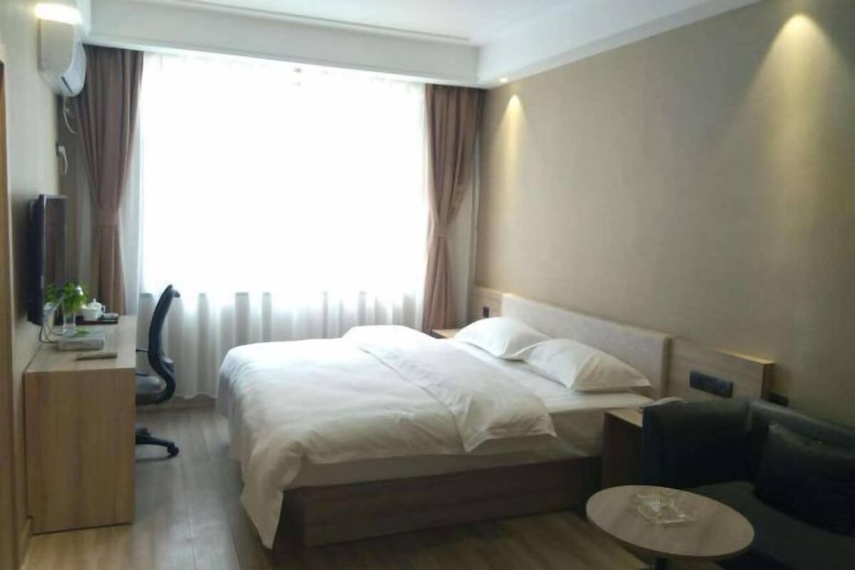 Une chambre d’hôtel avec un lit, un bureau, une chaise, une petite table et une fenêtre avec des rideaux.