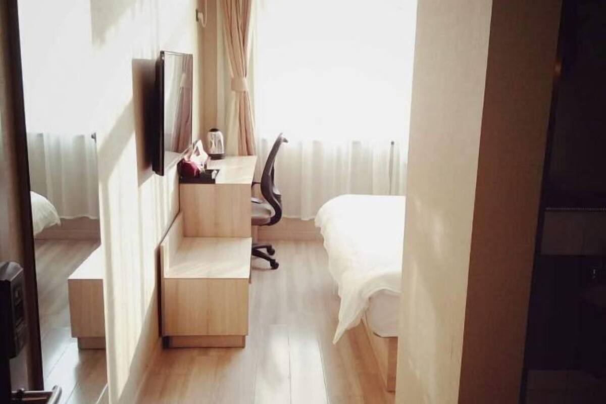 Une chambre d’hôtel comprenant un lit, un bureau avec une chaise, une télévision et une fenêtre avec des rideaux.
