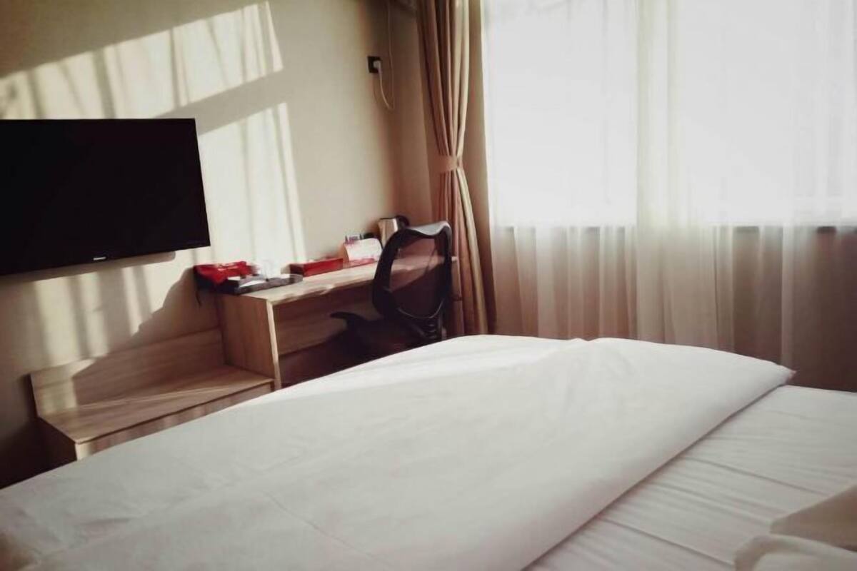 Une chambre d’hôtel avec un lit, un bureau, une chaise, une télévision et une fenêtre avec des rideaux.