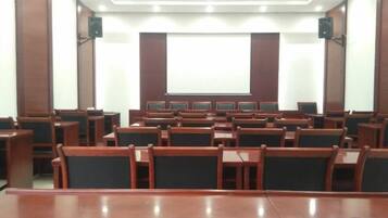 A conference room with rows of wooden chairs, a large table in the front, and a projection screen at the front.