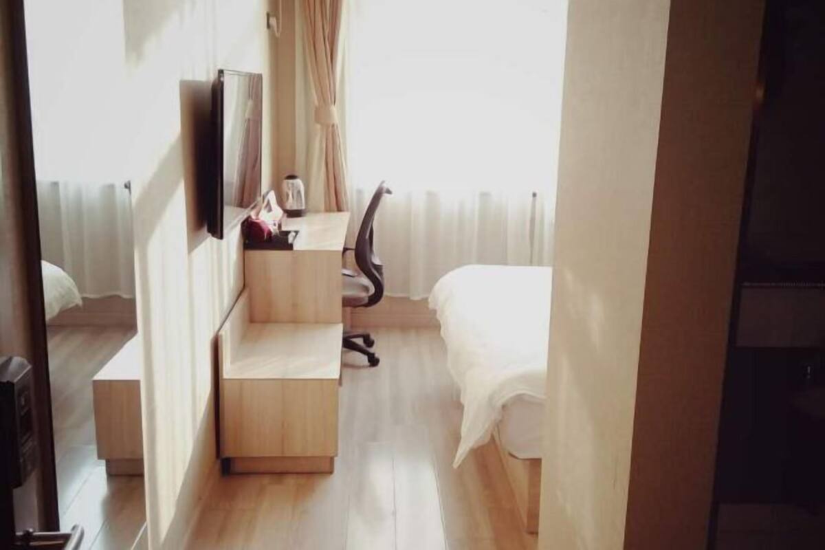 Une chambre d’hôtel de taille réduite, comprenant un bureau en bois, une chaise, un lit et un téléviseur fixé au mur.