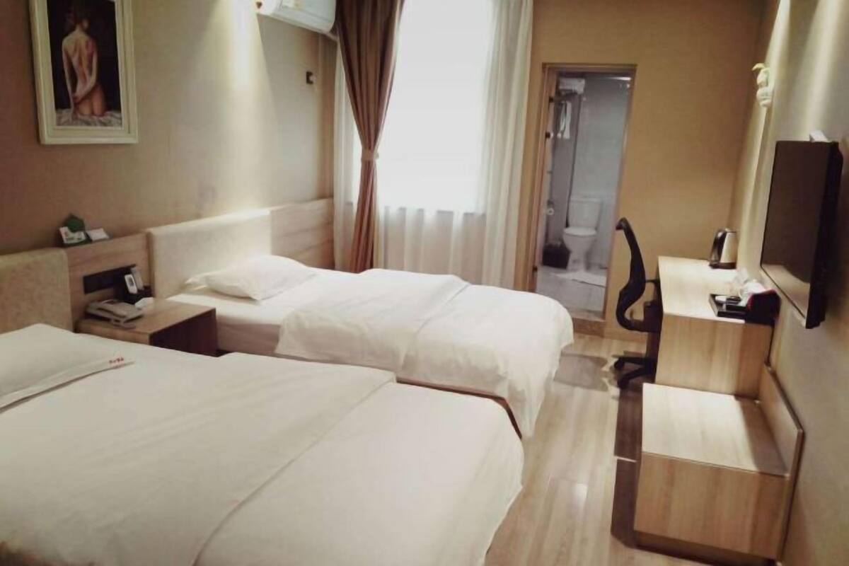 Une chambre d’hôtel avec deux lits, un bureau, une chaise, une télévision et un espace douche.