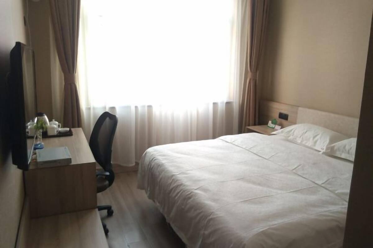 Une chambre d’hôtel comprenant un lit, un bureau avec une chaise, une table de chevet et une fenêtre avec des rideaux.