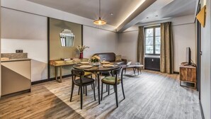 A modern dining area with a round table set for four, a sofa, and a large window with curtains. - Majestic Broadway - 4 star apartment with spectacular views (Chamonix-Mont-Blanc)
