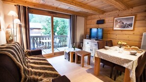 Ein gemütliches Blockhäuschen mit einer Couch, einem Esstisch und einem Fernseher.