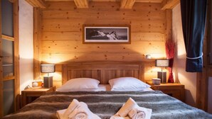 Ein gemütlicher Holzraum mit einem Bett, zwei Nachttischen, einem gerahmten Bild an der Wand und einem Fenster mit Vorhängen.