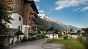 Eine Berghütte mit hölzernen Balkonen, einem Parkplatz und Blick auf schneebedeckte Berge.