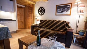 Ein gemütliches Wohnzimmer mit einer Couch, einem Couchtisch mit Flasche und Gläsern, einer Dartscheibe und einem gerahmten Bild an der Wand.