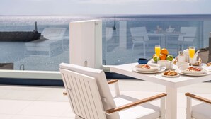 Varanda com mesa posta para o café da manhã, com vista para o mar, mostrando a costa e um farol.